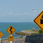 Steep and winding coastal road signs at Noen Nang Phaya viewpoint in Chanthaburi